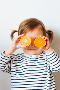 Toddler girl with orange slices over her face for EllyPop photoshoot
